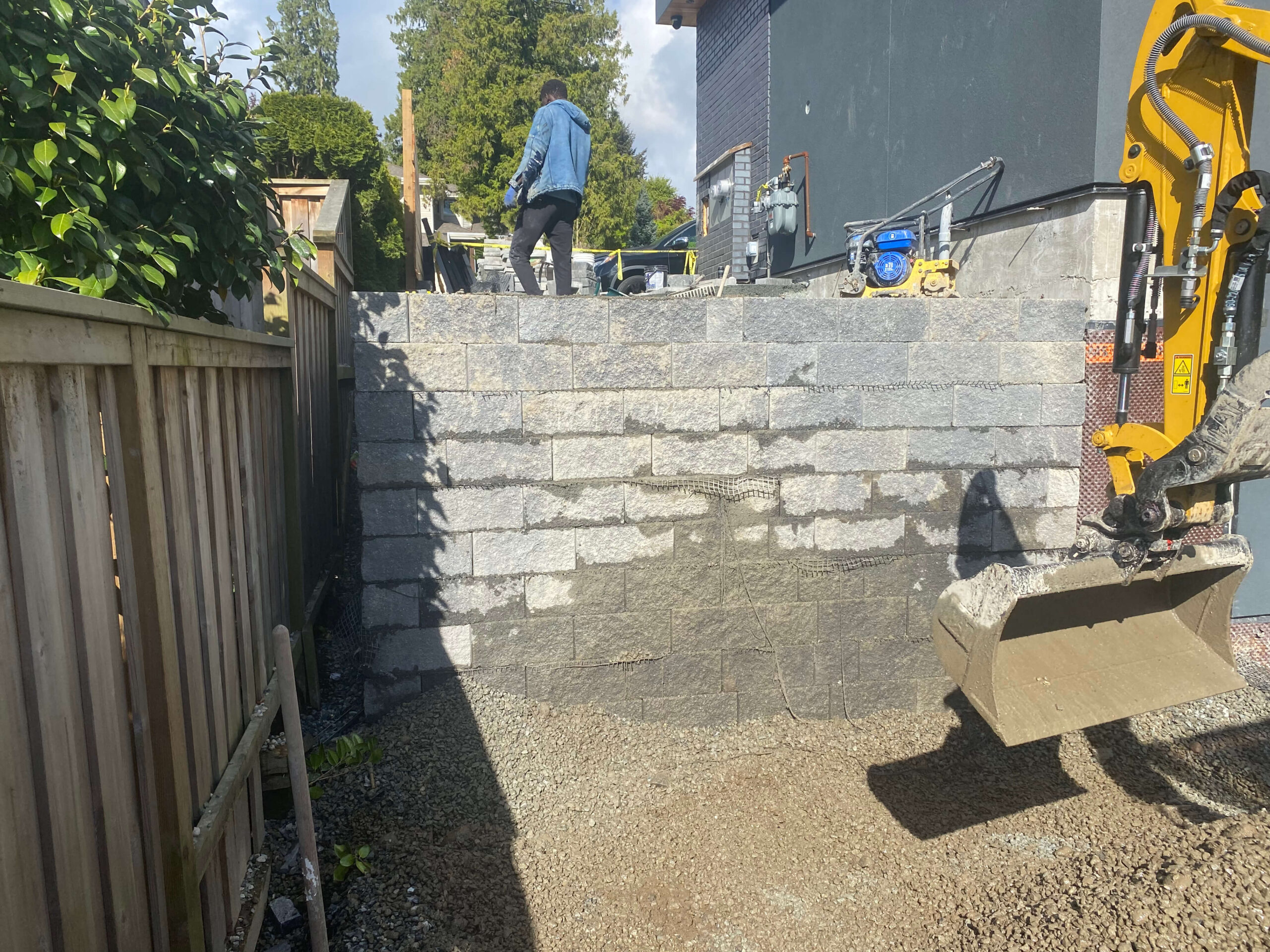 Large concrete block retaining wall under construction with excavator in Calgary backyard